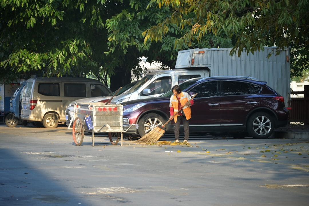 person-sweeping-street-near-parked-cars-plo2i1thm-a
